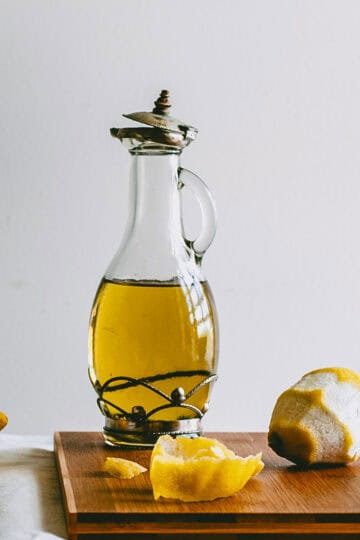 Glass bottle of lemon infused olive oil on a wooden board with peeled lemons.