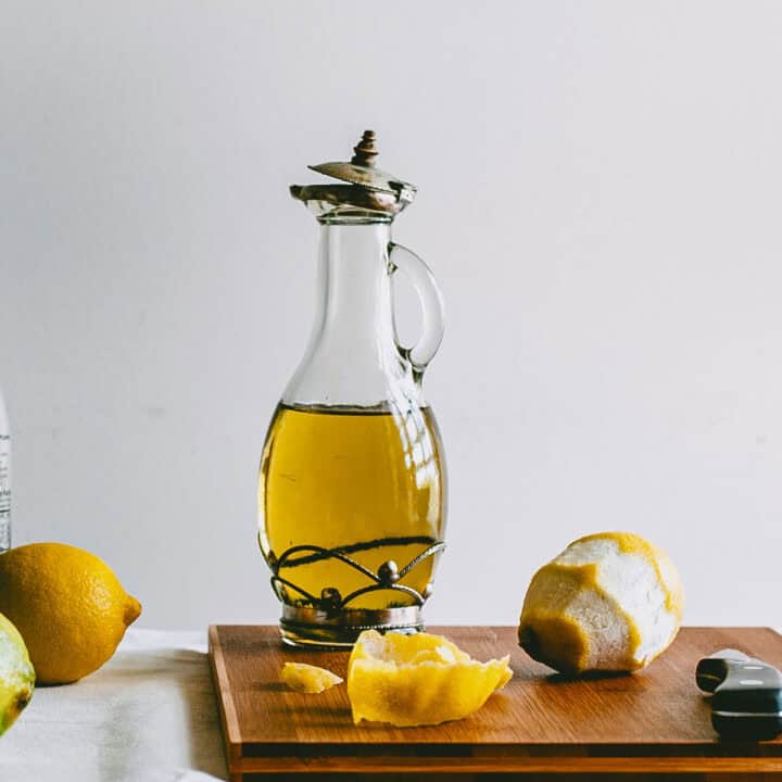 Glass bottle of lemon infused olive oil on a wooden board with peeled lemons.