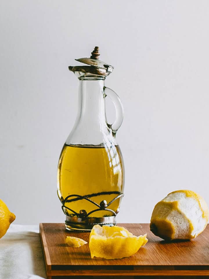 Glass bottle of lemon infused olive oil on a wooden board with peeled lemons.