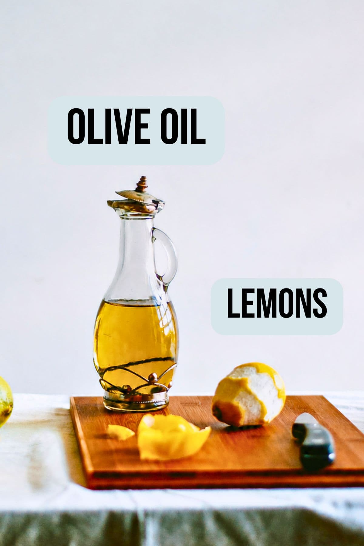 Bottle of olive oil and lemons on a wooden board labelled as ingredients for lemon infused olive oil.