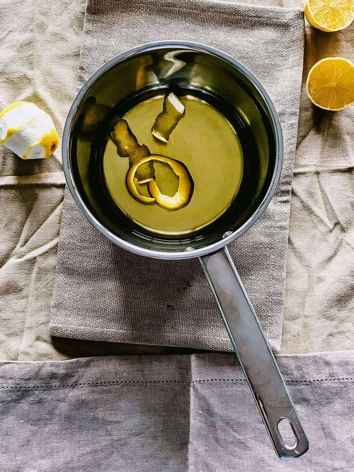 Overhead view of lemon peel infusing in olive oil in a stainless steel saucepan.