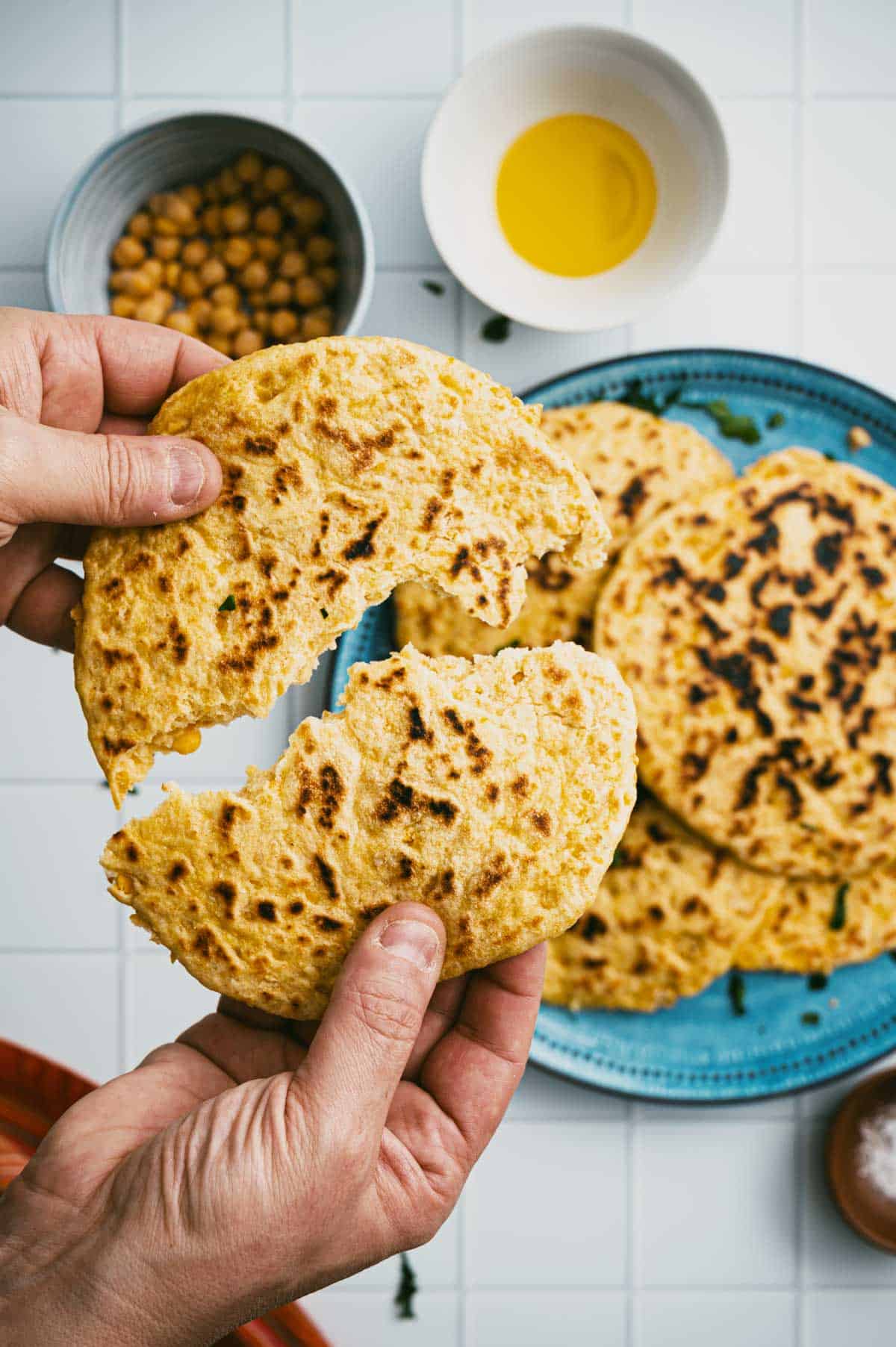 Hands tearing soft chickpea flatbread in half.